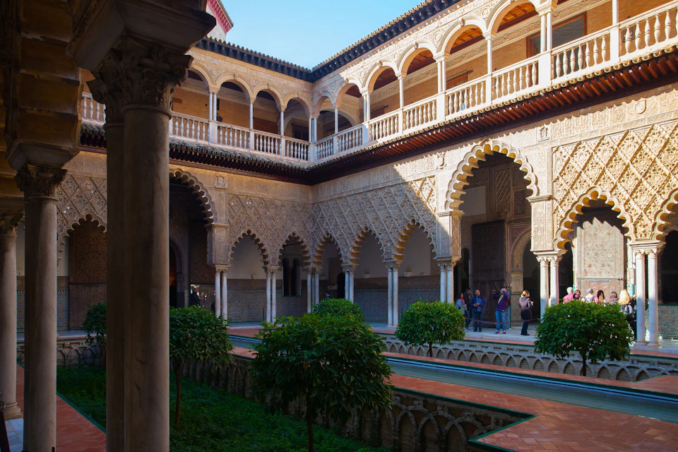 A courtyard with ornate arches, lush greenery, and people exploring the historic architectural surroundings.