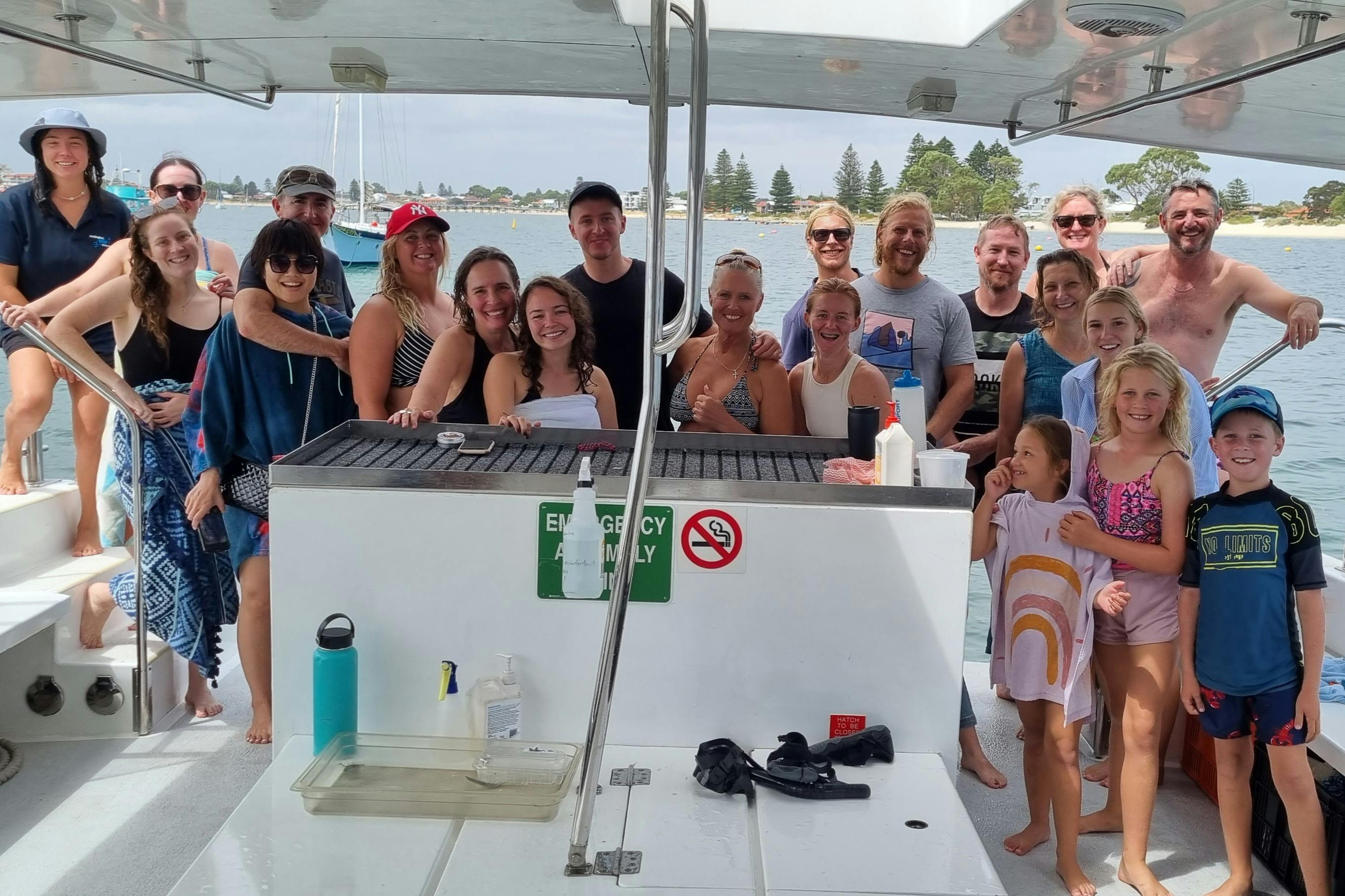 Μια ομάδα χαμογελαστών ανθρώπων σε μια βάρκα, με μια προκυμαία και δέντρα ορατά στο παρασκήνιο. Μια πινακίδα λέει "ΜΟΝΟ ΓΙΑ ΕΚΤΑΚΤΗ ΑΝΑΓΚΗ".