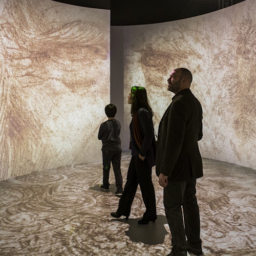 Three people stand in a room with large, curved projections of a detailed, textured image, possibly artwork, covering the walls and floor.