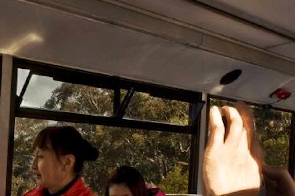 Passengers sitting inside a bus with colorful seats, large windows showing a scenic mountainous view with trees.