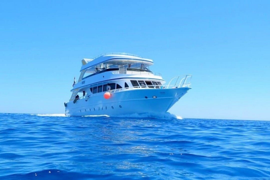 A white yacht sailing on clear blue water under a bright blue sky with a visible orange buoy on its side.