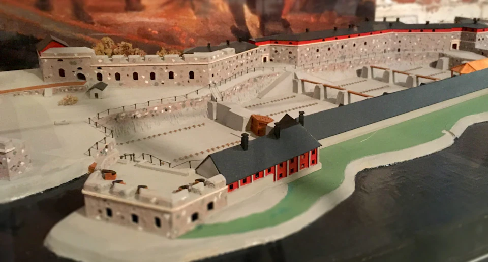 Model of an old fortress with multiple stone buildings and walls, featuring pathways and red-roofed structures.