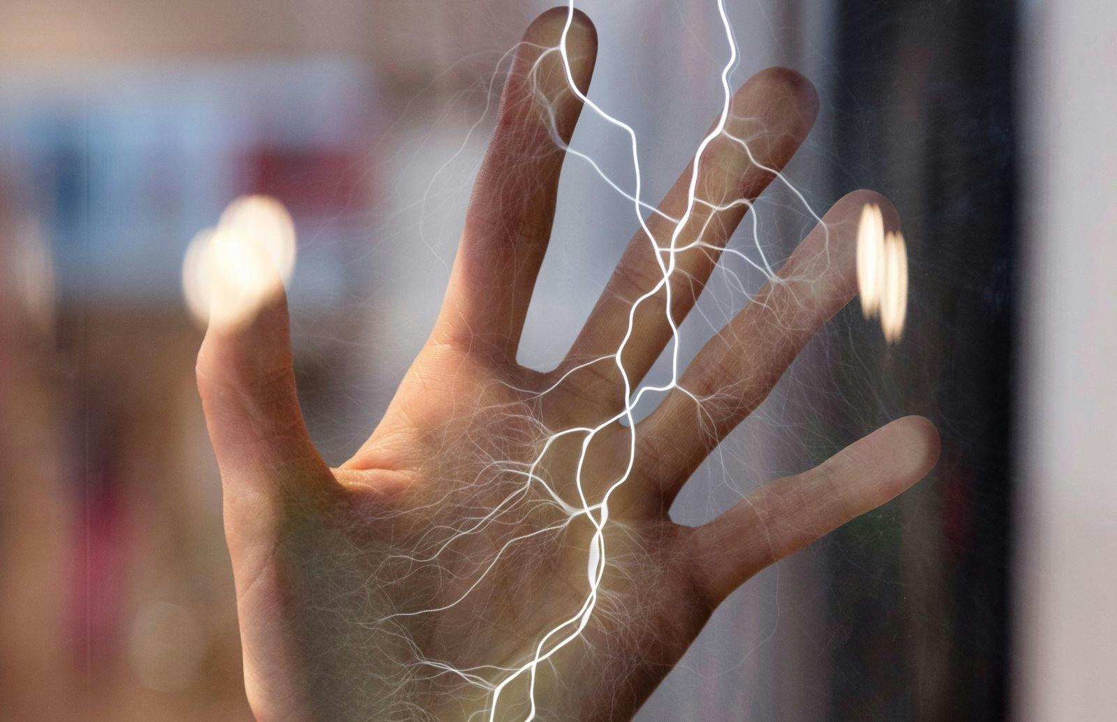 Ett handberörande glas med synliga strömmar av elektricitet som rinner genom och runt det. Suddig bakgrund.
