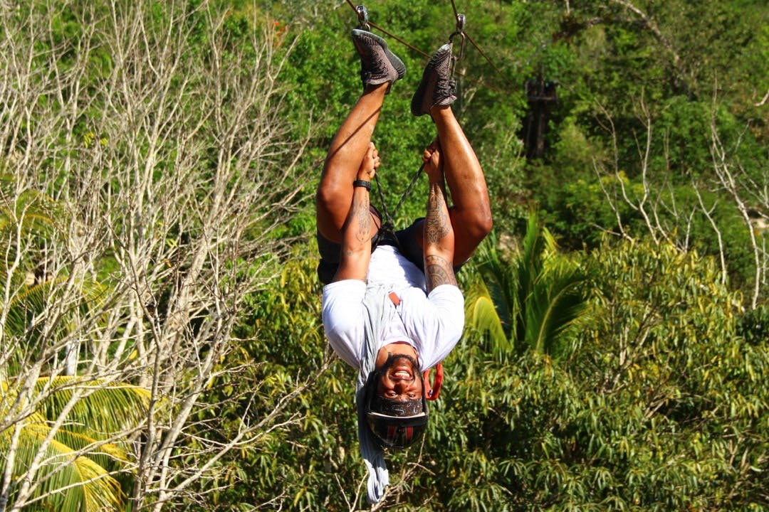 Une personne fait de la tyrolienne à l'envers, avec un large sourire, entourée d'arbres verdoyants.