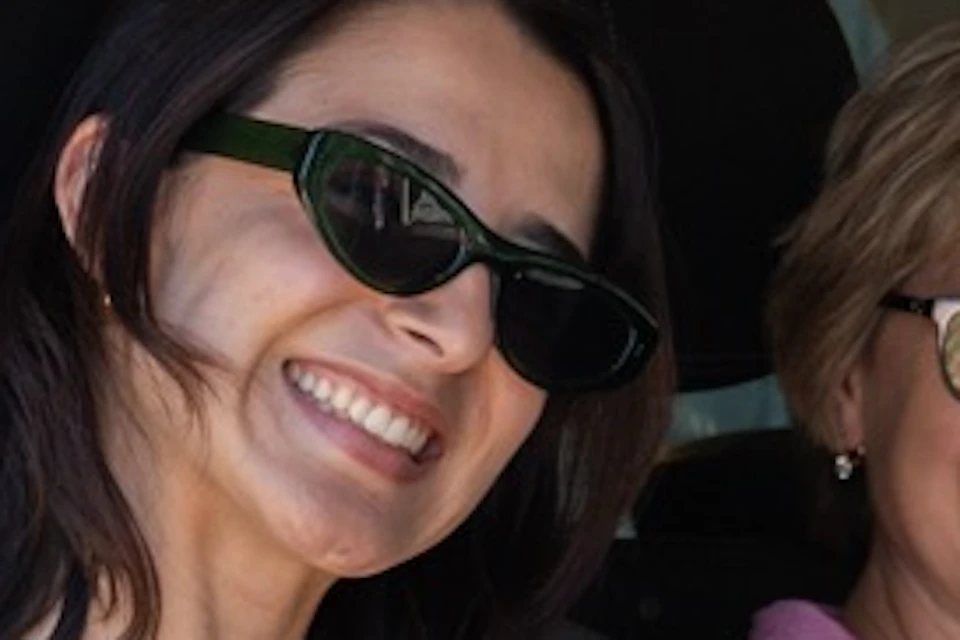 Four people seated inside a car, with a woman in the front seat waving and smiling at the camera.