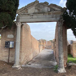 Forntida stenvalv med två pelare, som leder till en ruin med tegelväggar och en skylt med ”Domvs Del Brvtto”.