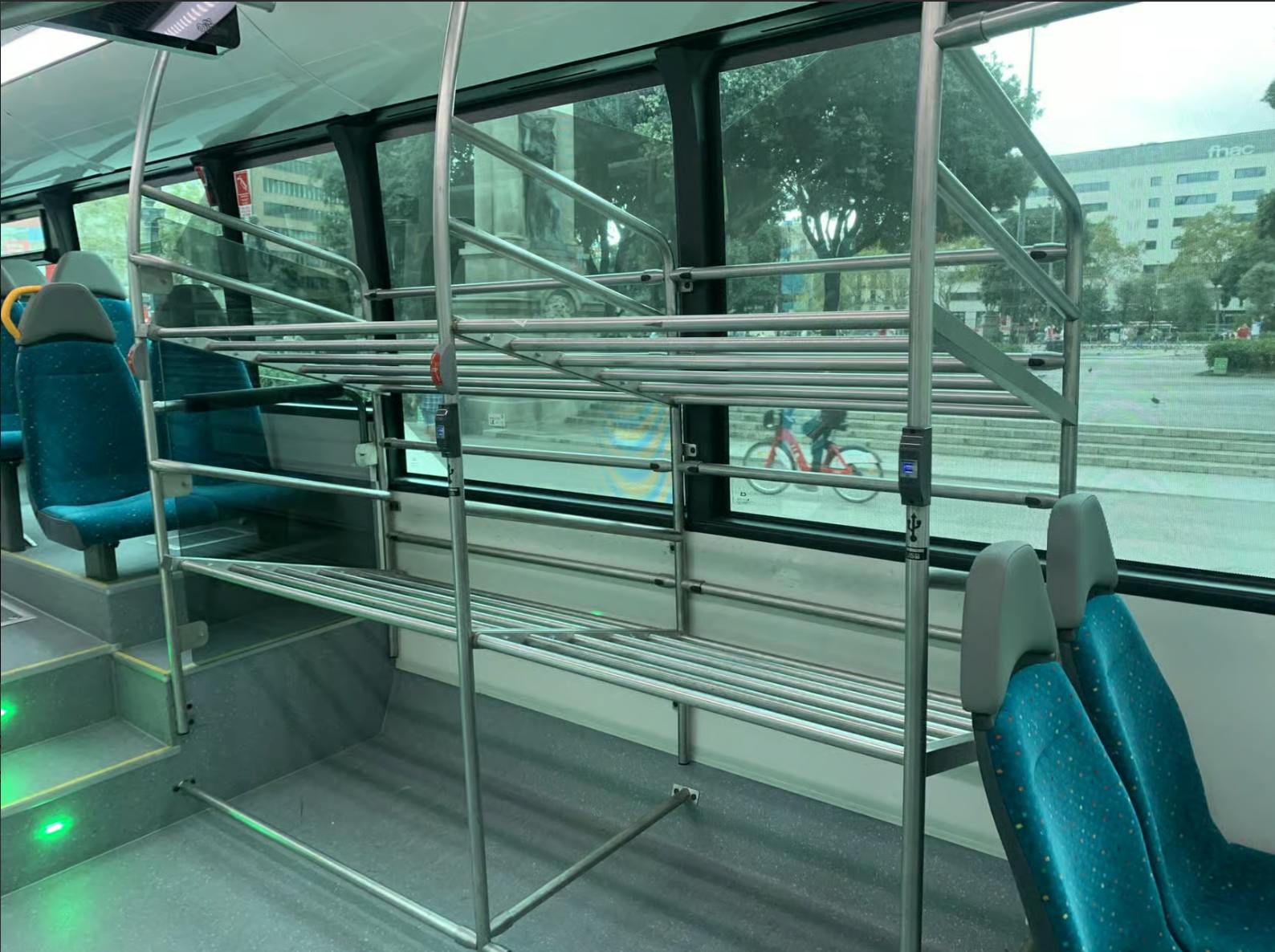 Intérieur d'un bus avec des porte-bagages en métal, des sièges à motifs bleus et une vue sur les rues de la ville à travers de grandes fenêtres.