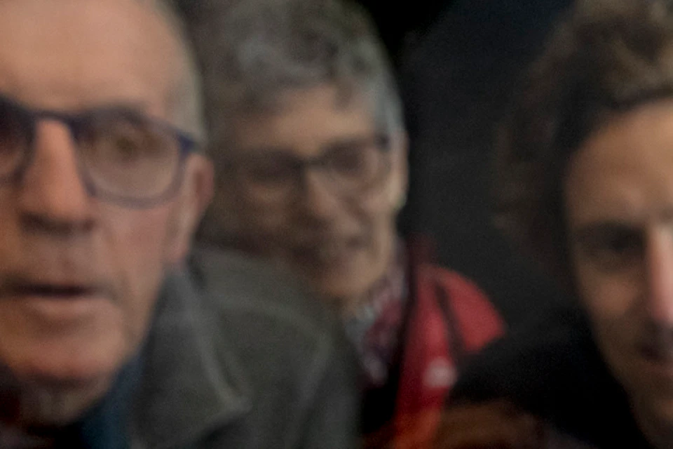 Three people leaning forward and looking through a transparent surface, with their reflections visible.