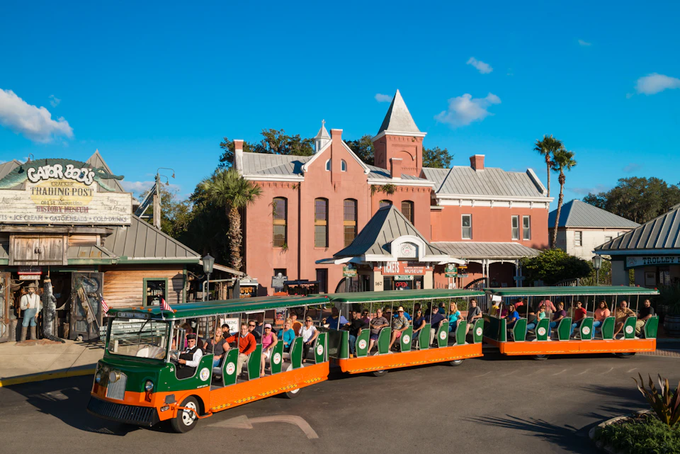 Tourist tram with passengers in front of a historic brick building with turrets on a sunny day.