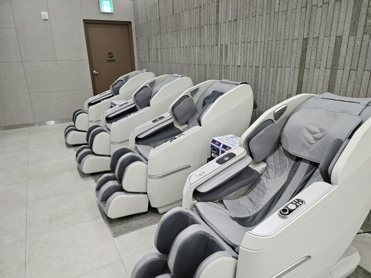A row of white and gray massage chairs in a modern interior space with a textured wall and a door in the background.