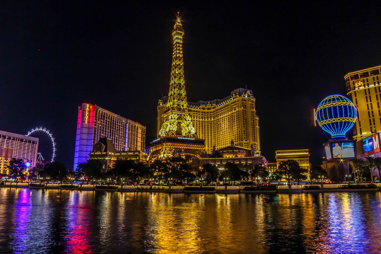 这张照片展示了夜间明亮的埃菲尔铁塔复制品，周围环绕着光线充足的建筑物，水体上有反光。