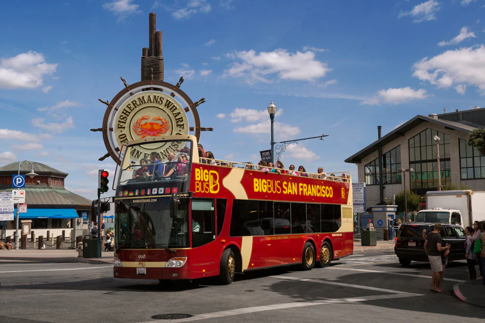 Double-decker tour bus labeled "Big Bus San Francisco" passing by the Fisherman's Wharf sign on a sunny day.