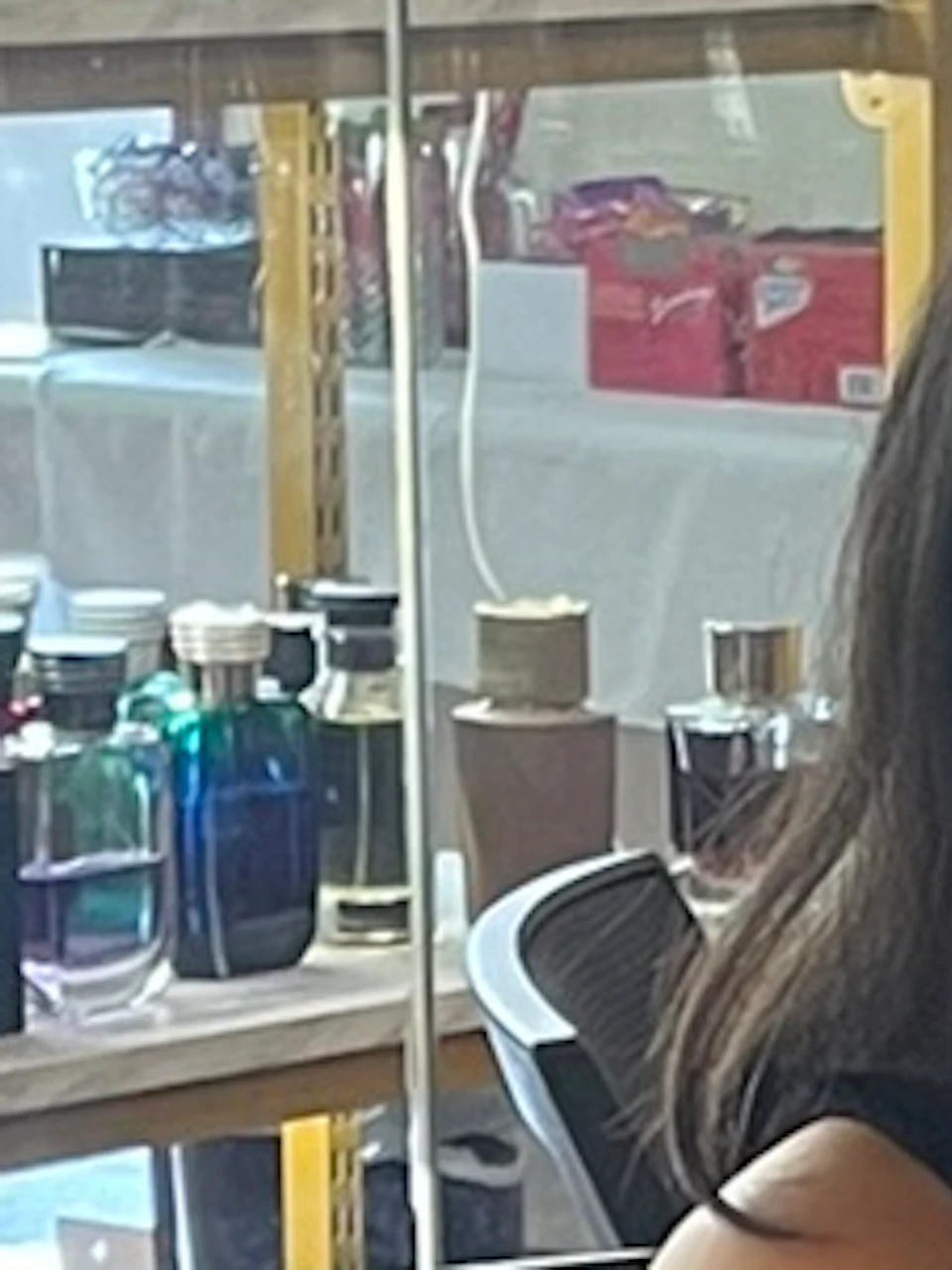 Two people seated at a table in a perfume shop. One is smelling a fragrance strip, with rows of bottles in front of them.