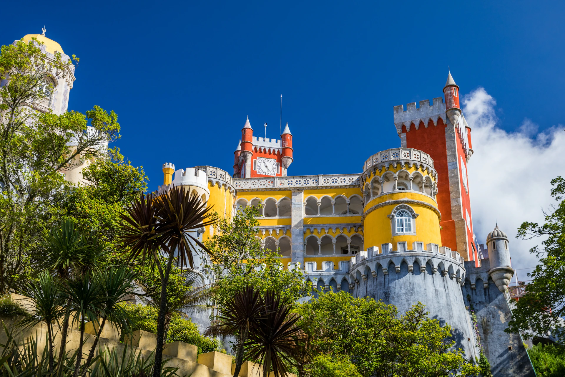 A colorful castle with yellow, red, and white walls surrounded by trees under a clear blue sky.