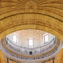 Invändig bild av ett kupoltak med utsmyckade stenbågar och rektangulära fönster, omgivet av en cirkulär balkong.