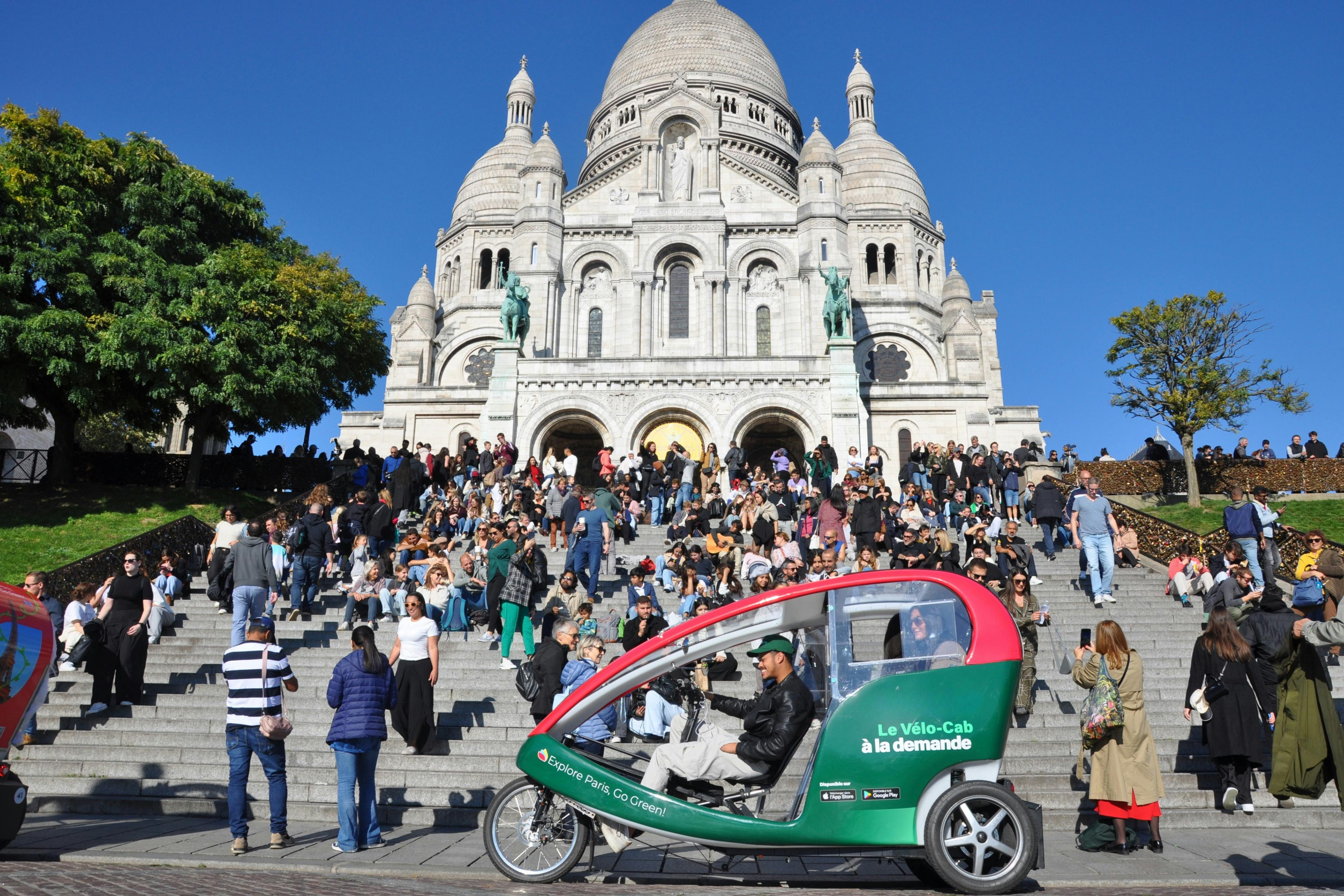 Crowded steps leading to the Sacré-Cœur Basilica in Paris, with a green and red pedicab in the foreground.