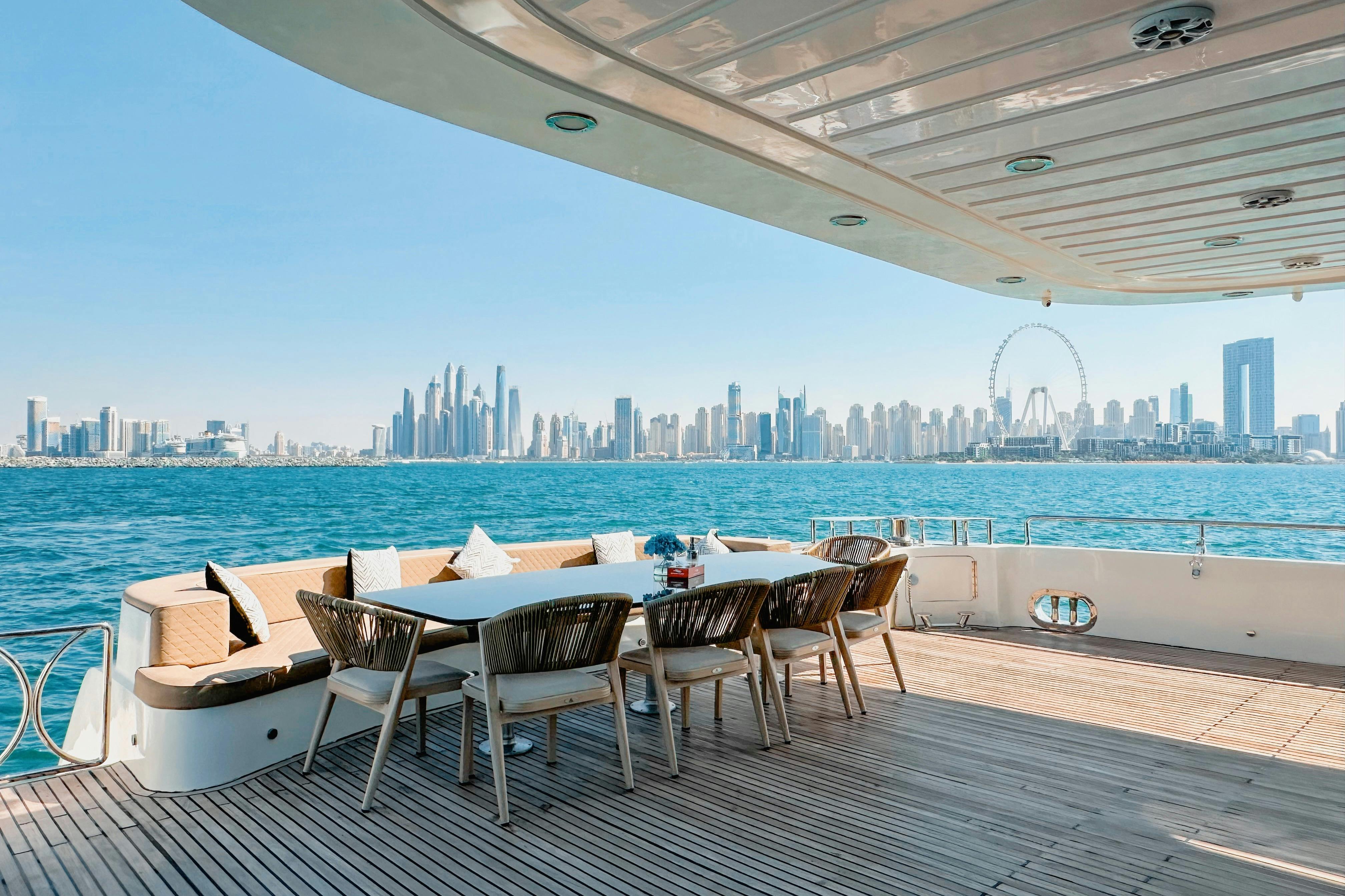 Venkovní jídelní kout na jachtě s proutěnými židlemi a stolem s výhledem na panorama města a velkým vyhlídkovým kolem přes vodu.