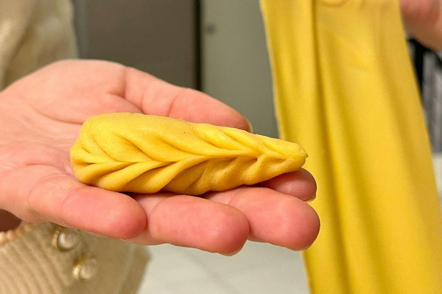A hand holding a small, yellow, leaf-shaped piece of dough with intricate detailing.