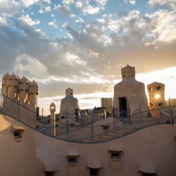 Nyfiken takarkitektur med böjda, strukturerade skorstenar och ventiler under en molnig himmel under solnedgången.