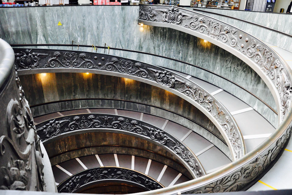 A spiraling staircase with ornate decorations and a polished finish, surrounded by a marble-like wall.