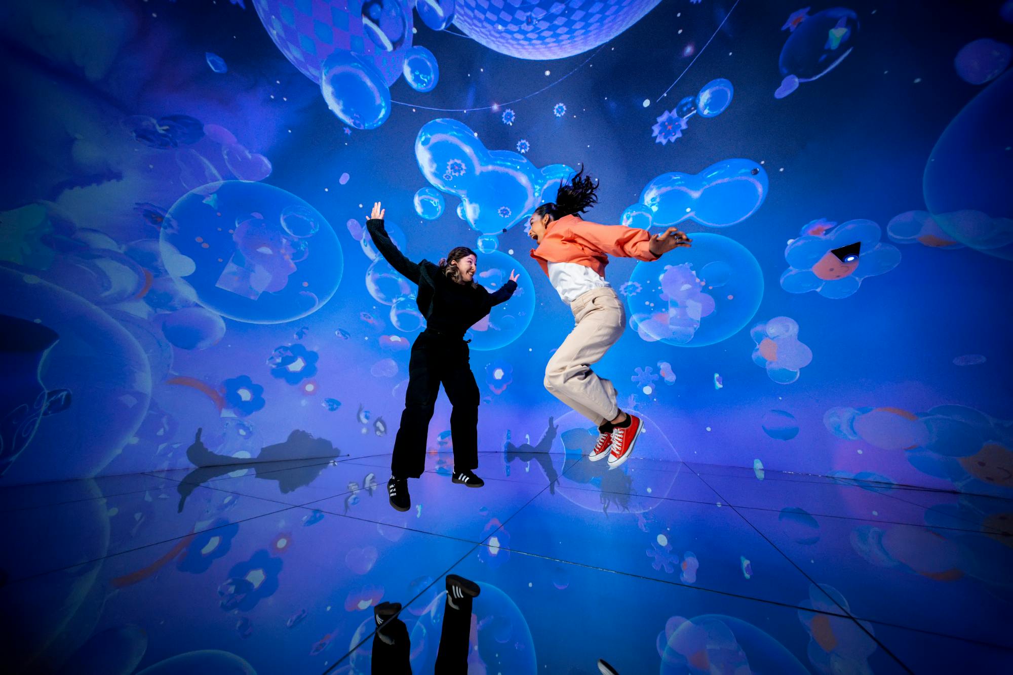 Dwie osoby wskakują w żywe, niebieskie, wciągające doświadczenie z motywem bąbelków.