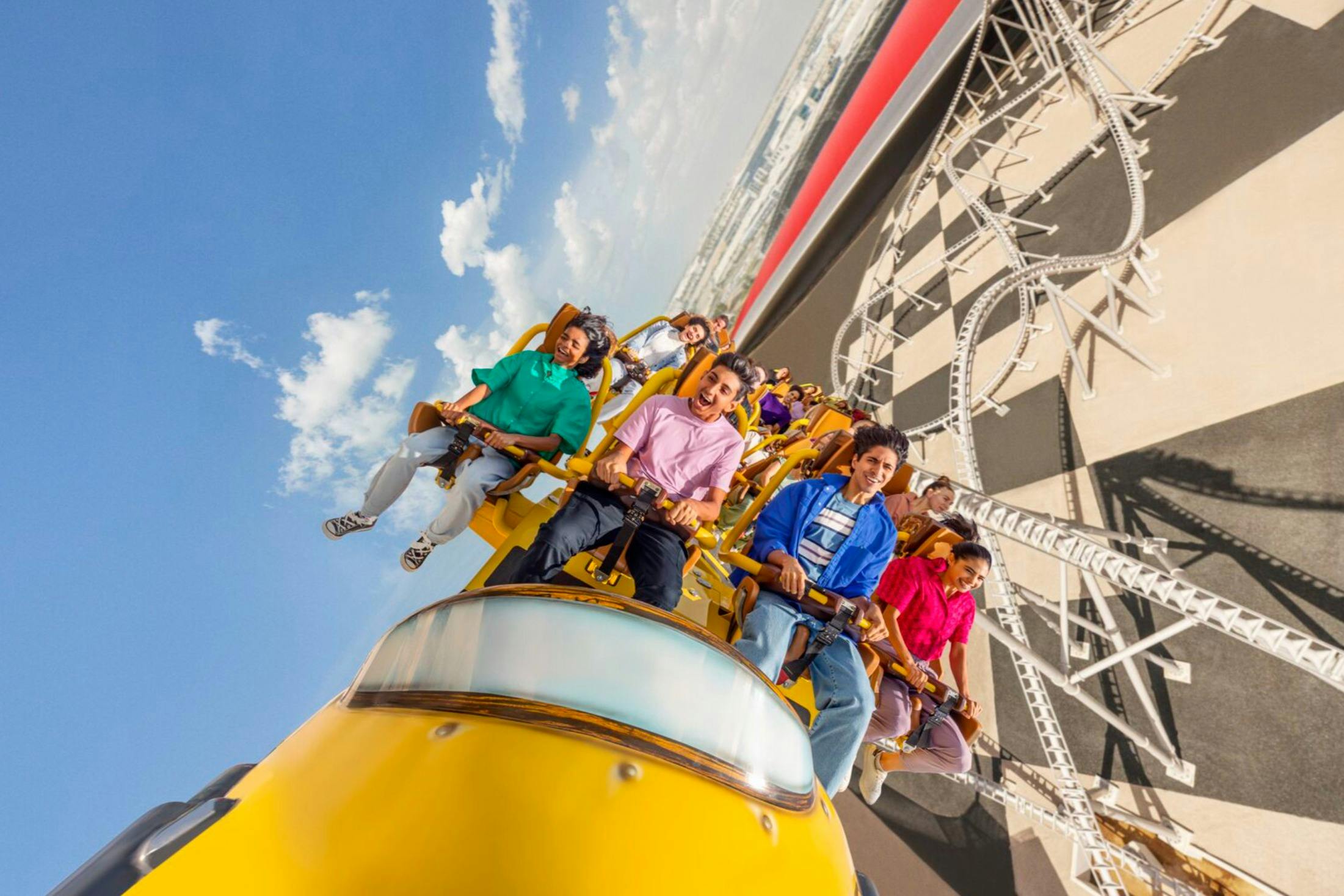 青い空の下で、黄色いジェットコースターに乗って、目に見える軌跡と建物を背景にした人々。
