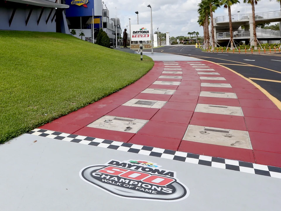 A red and white checkered walkway with handprints and signatures, labeled "Daytona 500 Champions Walk of Fame," at a motorsport venue.