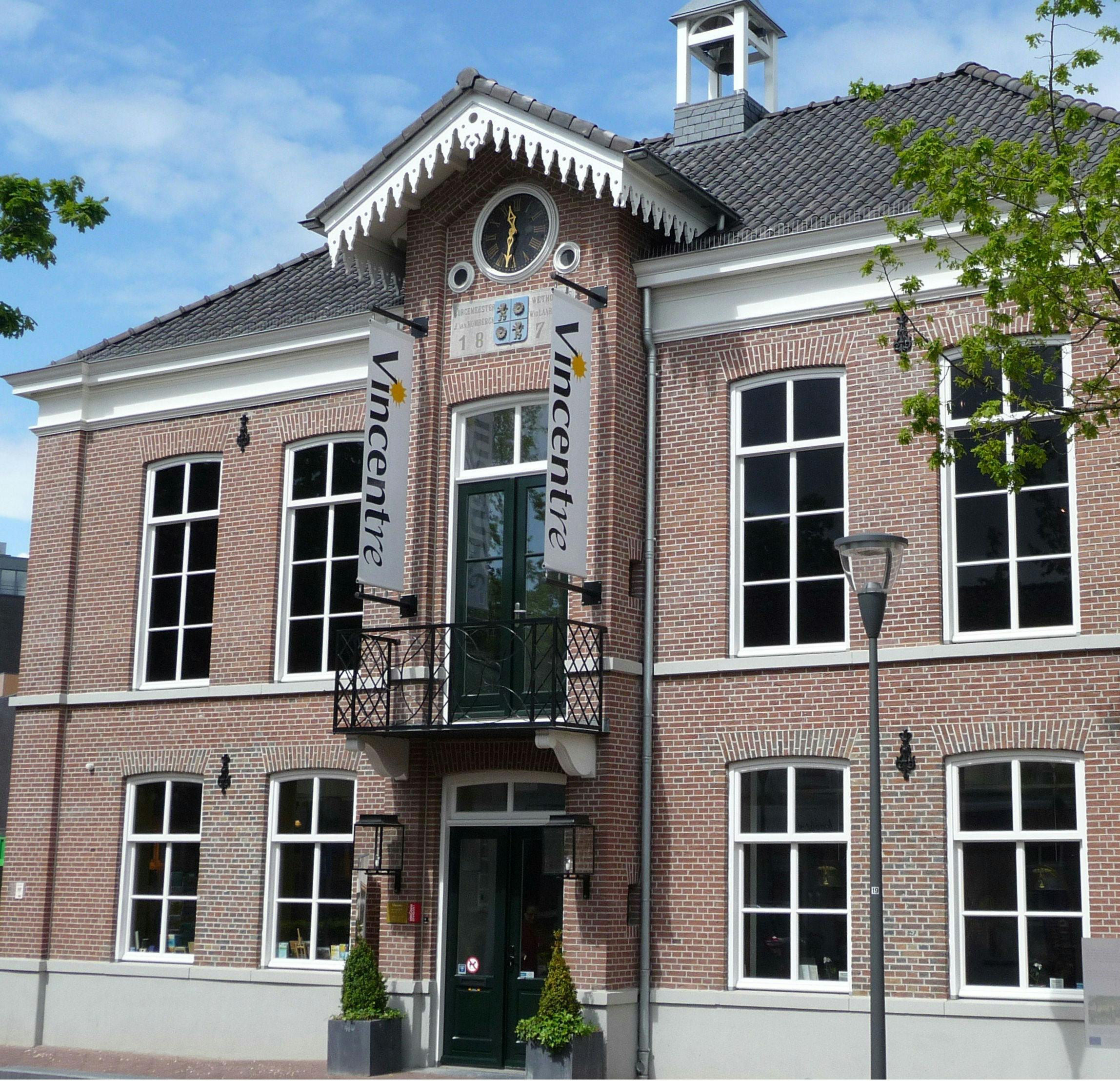 Brick building with large windows, a small balcony, and "Vincentre" banners. Trees frame the scene under a blue sky.