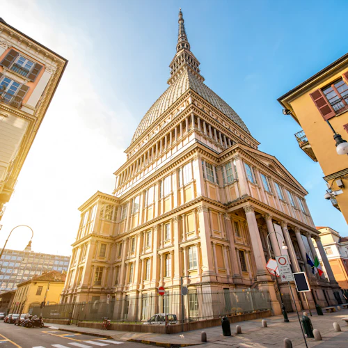 Utsmyckad byggnad med en hög spiral omgiven av äldre strukturer, sedd från en låg vinkel, under en klarblå himmel.
