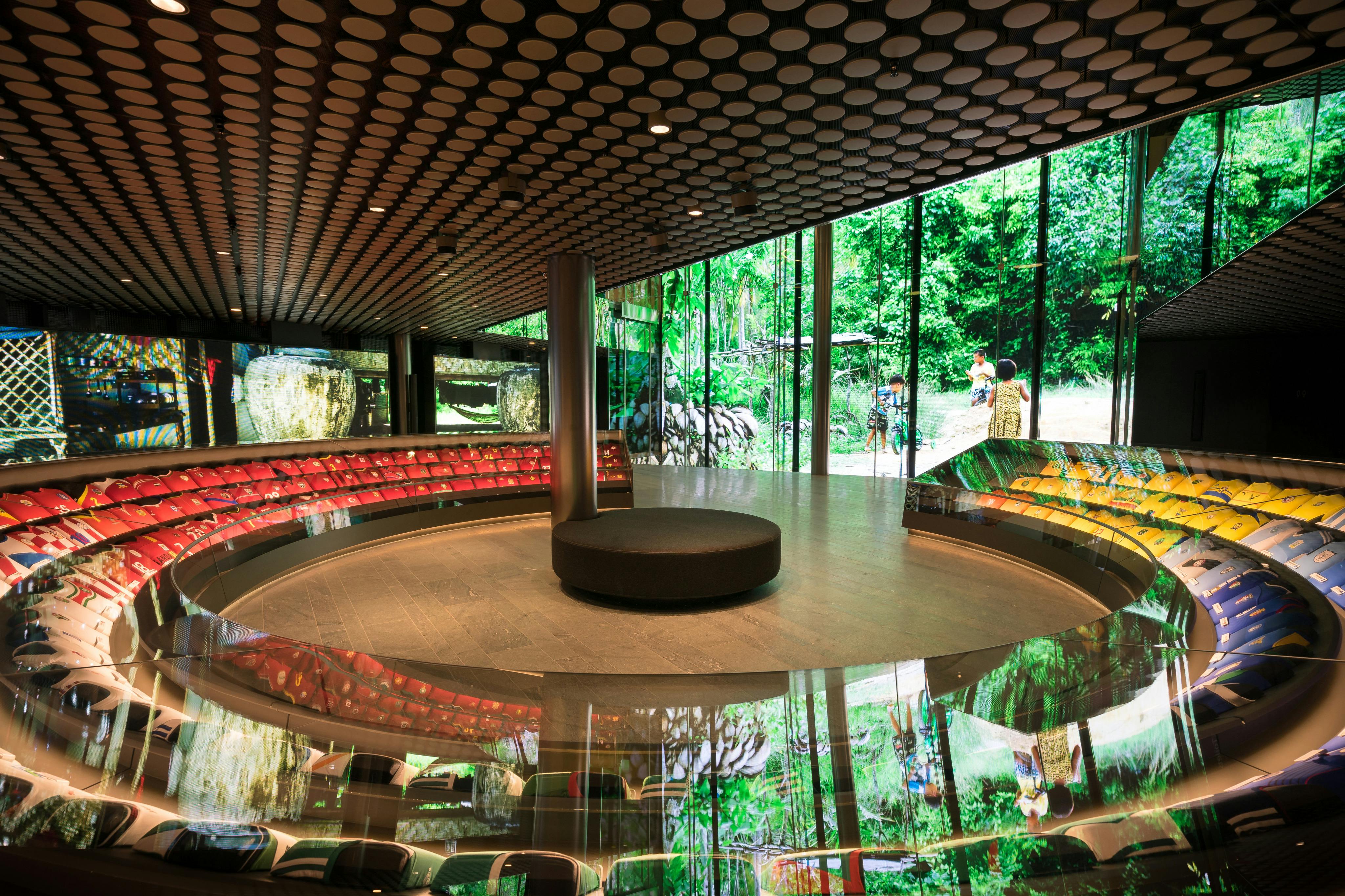 Современное круглое внутреннее пространство с большими цифровыми экранами, отображающими природные пейзажи, и мягкими скамейками по периметру.