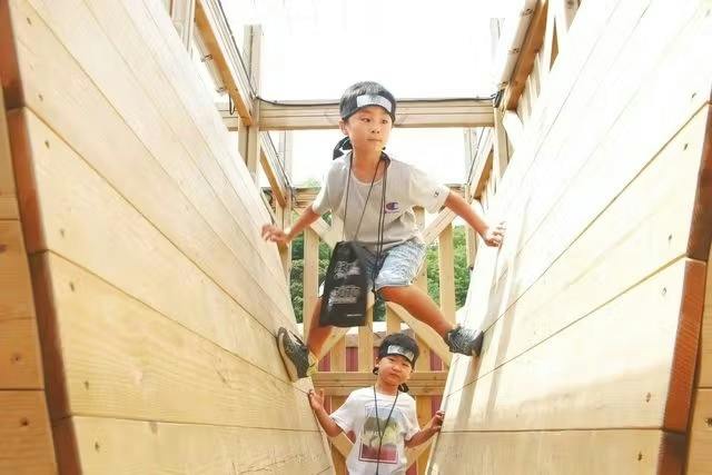 Two children climbing and balancing between wooden walls in an outdoor setting.