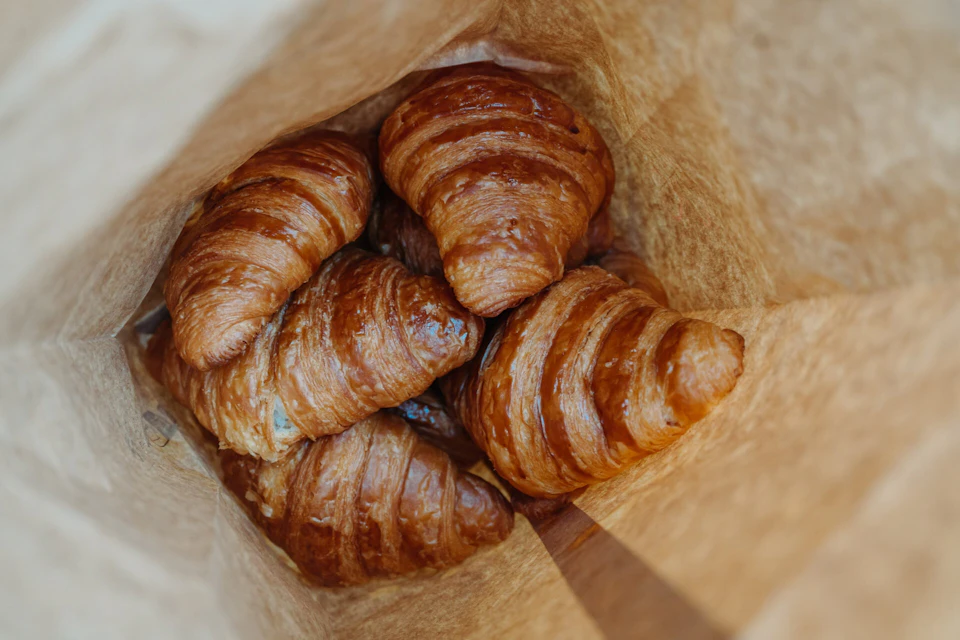 Several golden-brown croissants inside a paper bag, viewed from above.