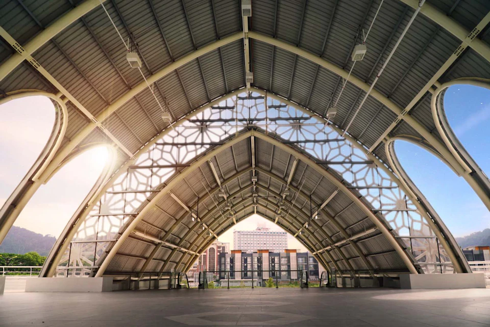 Interior of a modern arched structure with a geometric patterned wall, overlooking a cityscape in the background.