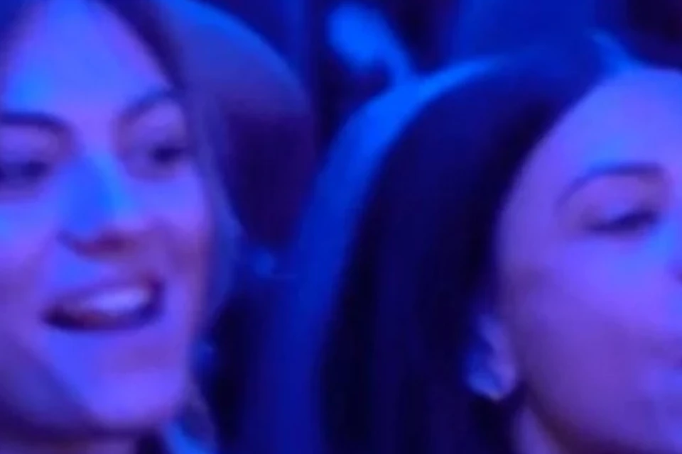 A group of people on a bus or train, illuminated by blue lighting, some appear to be talking and enjoying the ride.