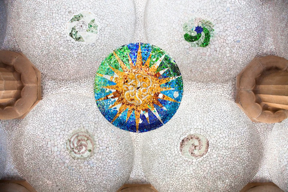 Mosaic ceiling featuring a central sun design surrounded by four spiral patterns, set against a white, textured background.