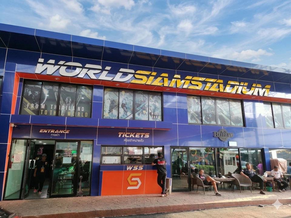 A blue building labeled "World Siam Stadium" with ticket counters and people outside on a sunny day.