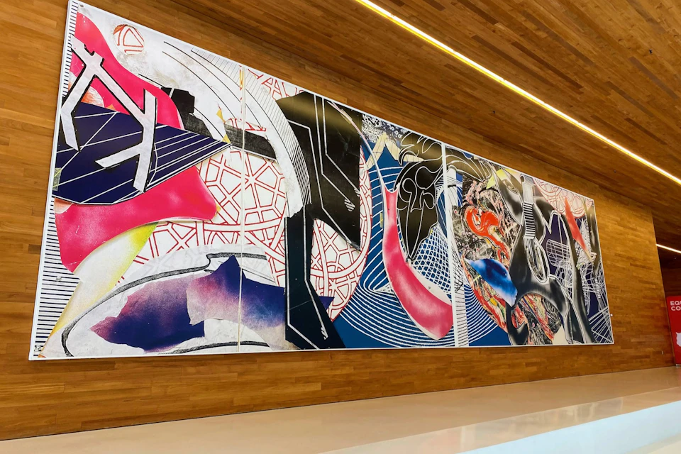 A large, colorful abstract mural with geometric patterns and shapes on a wooden wall inside a modern, well-lit space.
