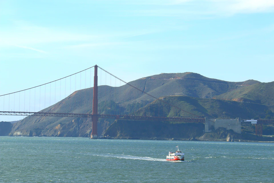 A boat on water with the Golden Gate Bridge and a hilly landscape in the background under a clear sky.