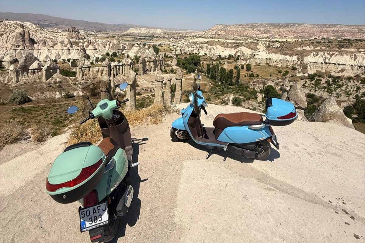 两辆蓝色和棕色滑板车停在悬崖上，俯瞰着多岩石的山地景观，植被稀疏。