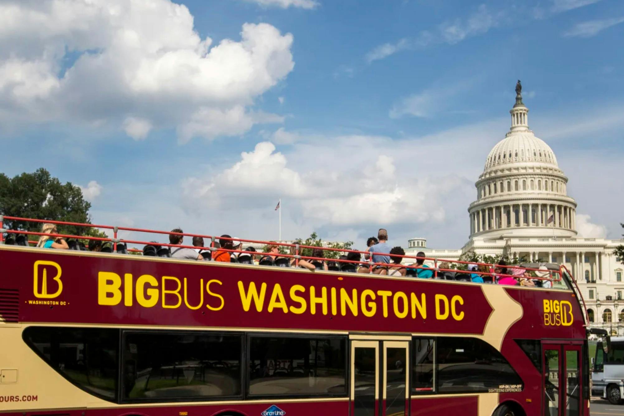 A double-decker tour bus labeled 'Big Bus Washington DC' with passengers, passing by the U.S. Capitol on a sunny day.