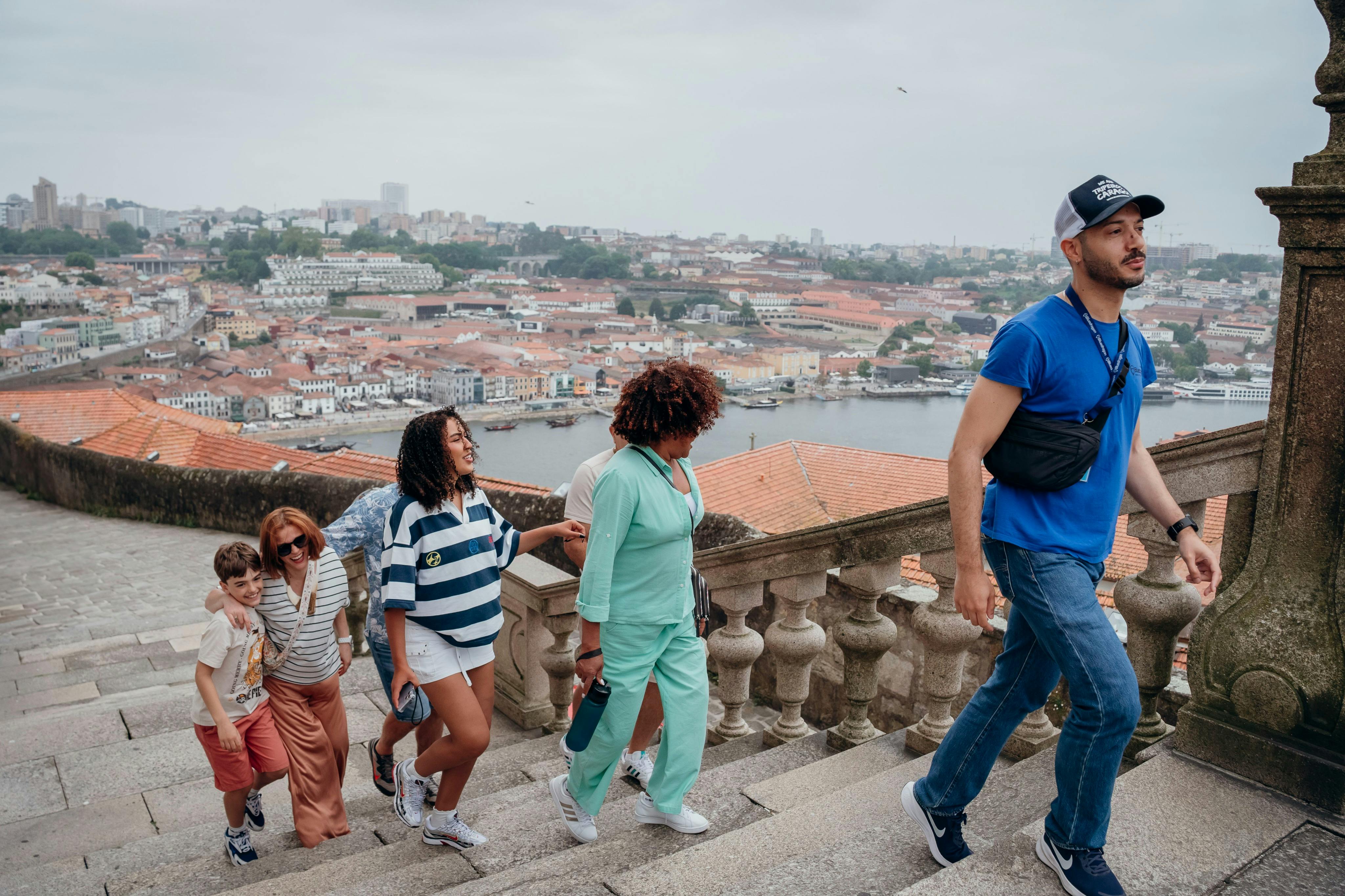 캐주얼한 옷을 입은 한 남성이 도시 풍경과 강을 배경으로 두 여성을 돌 계단으로 안내합니다.