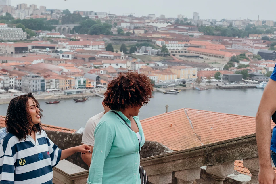 A man in casual clothes leads two women up stone steps, with a cityscape and river in the background.