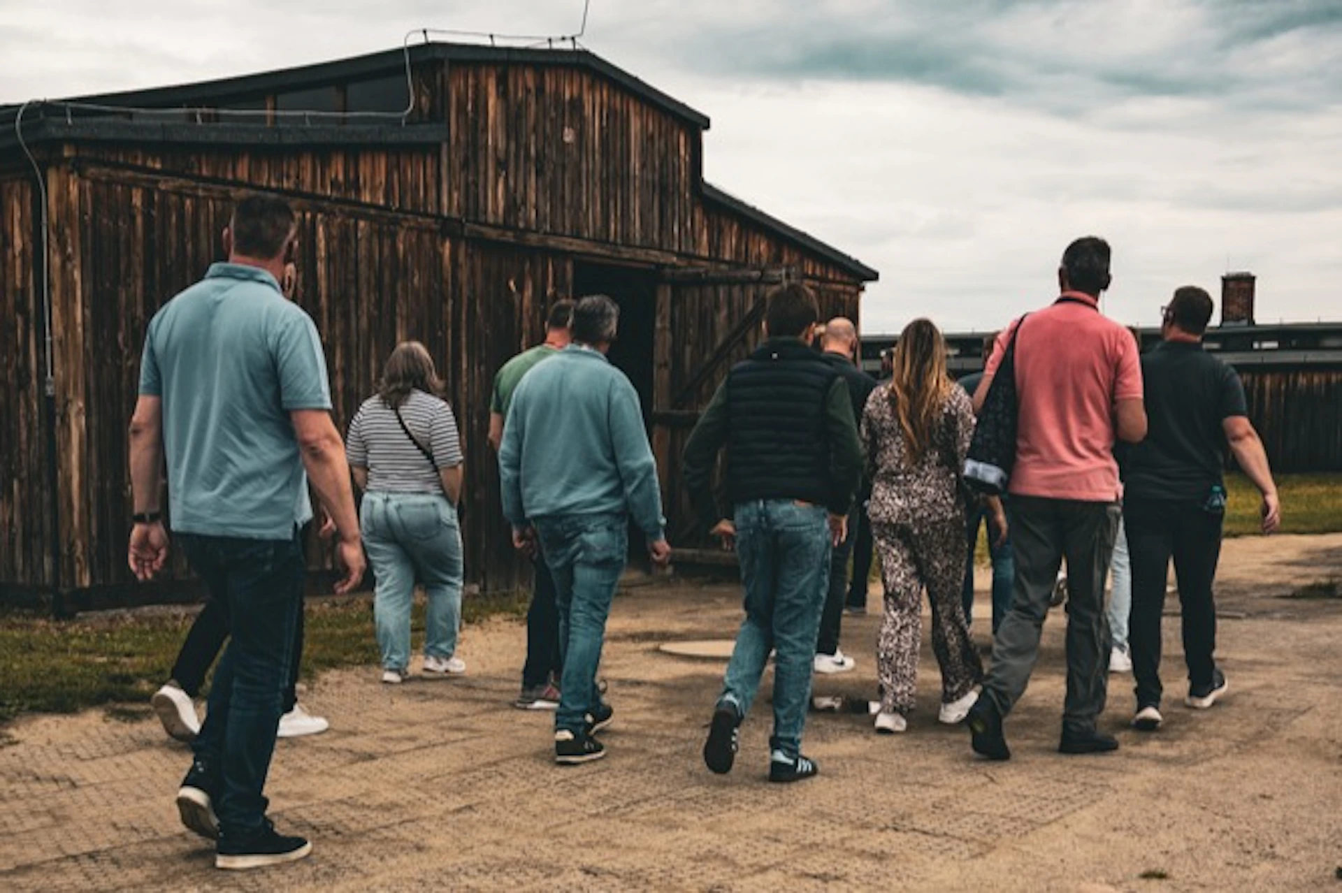 A group of people walking towards a weathered wooden building on a cloudy day.