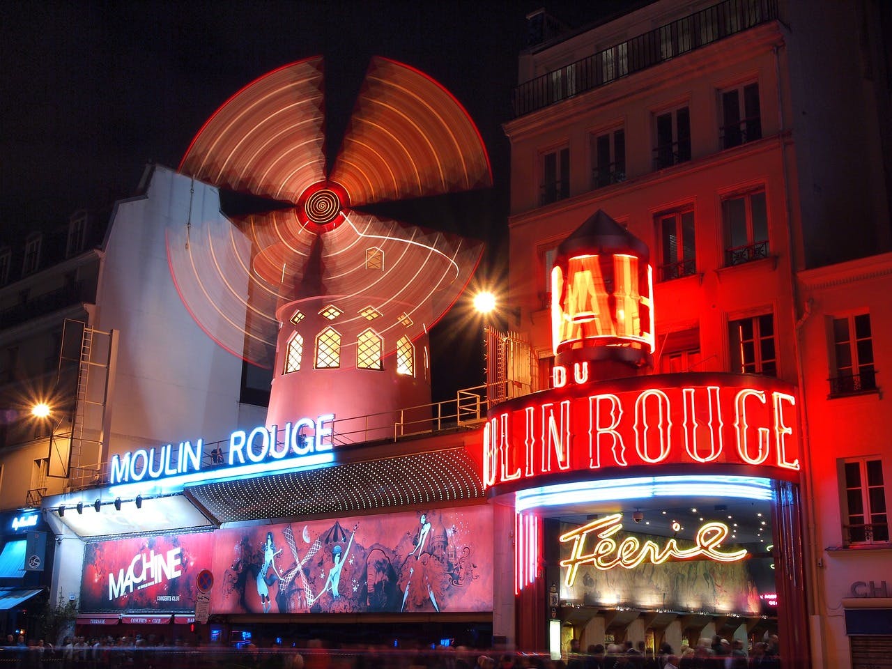 The Moulin Rouge in Paris at night, featuring its illuminated red windmill and vibrant neon signage.