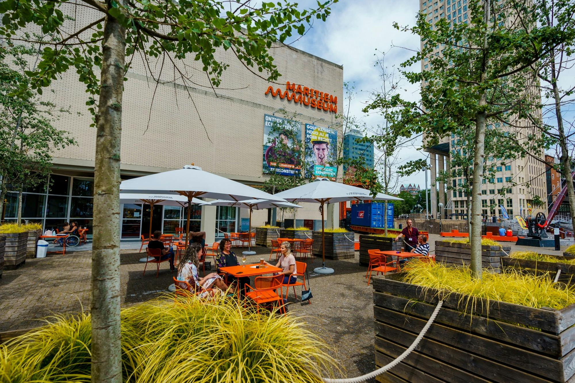 室外休息区设有橙色椅子和白色雨伞，位于一栋标有「艺术博物馆」的现代建筑前。