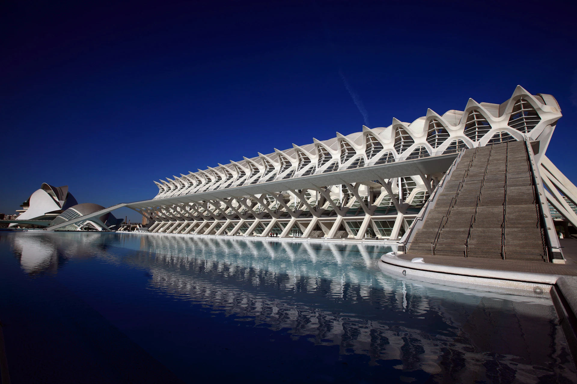 Modern white architectural structure with reflective pool in front and deep blue sky above.