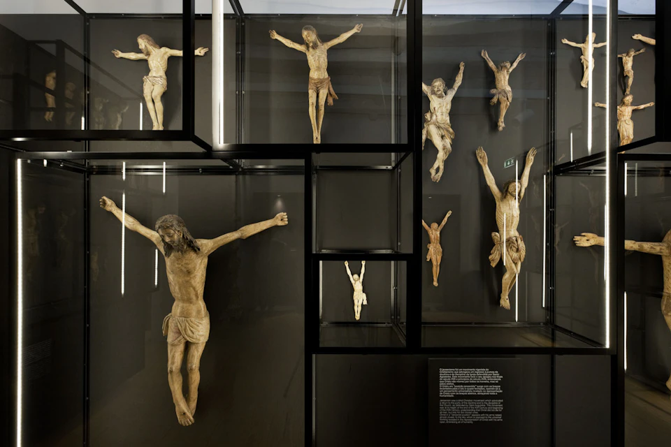 Nine crucifix sculptures of Jesus displayed in a glass case, each varying in size and pose.