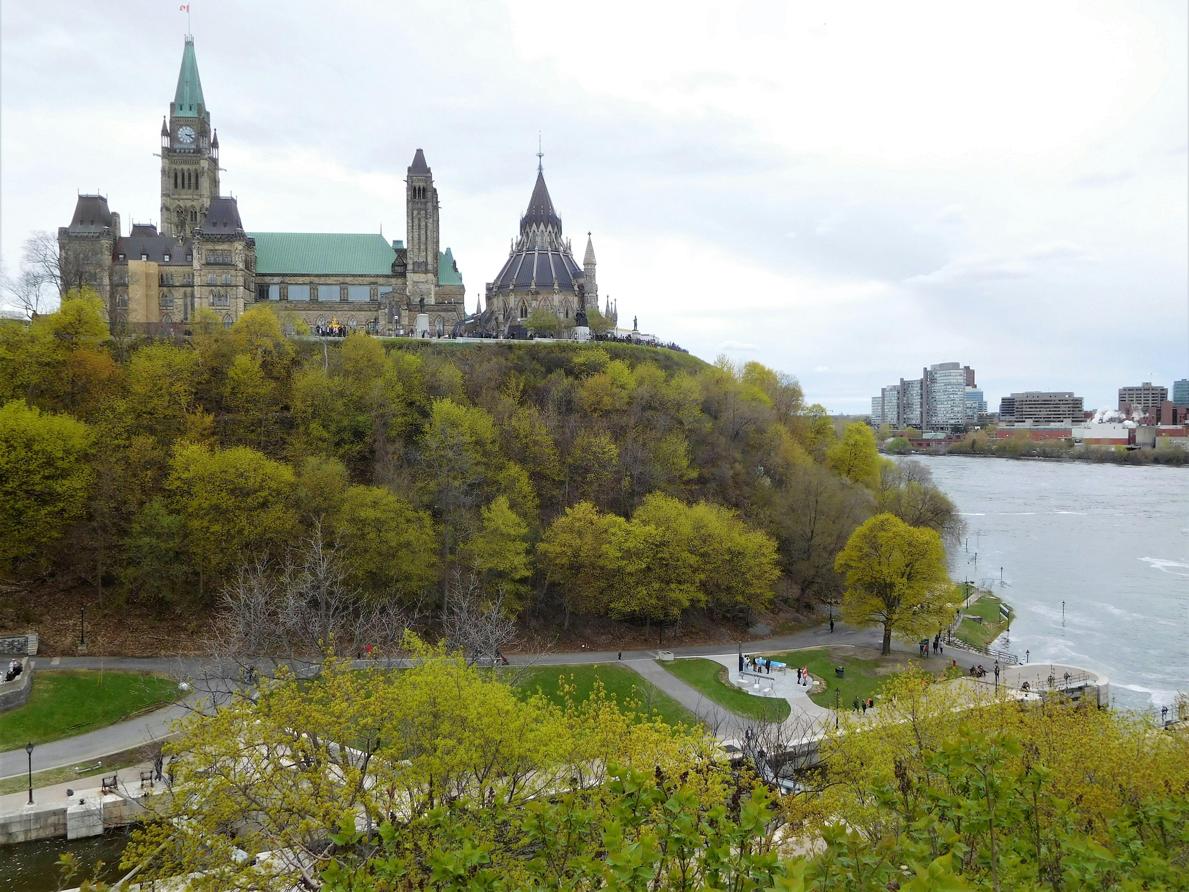 Bâtiments historiques au sommet d'une grande colline avec des arbres luxuriants, à côté d'une rivière et de bâtiments urbains modernes en arrière-plan.