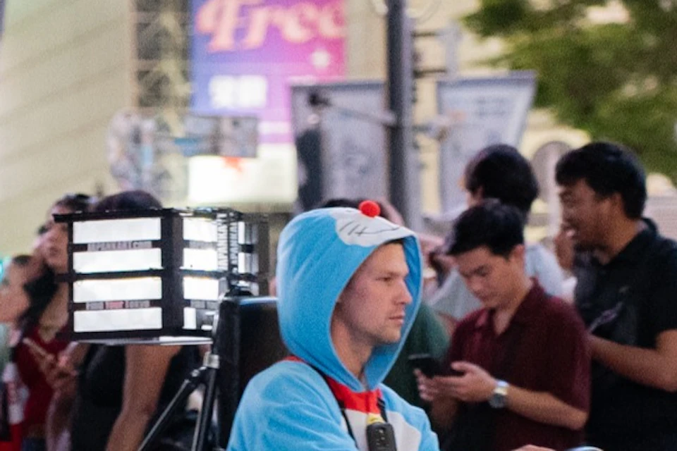 A person in a blue costume driving a go-kart through a busy crosswalk in an urban area at night.