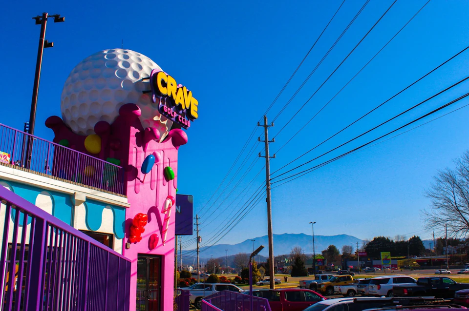 Exterior of the Crave Golf Club building with a giant golf ball structure, colorful decor, and surrounding power lines under a clear blue sky.